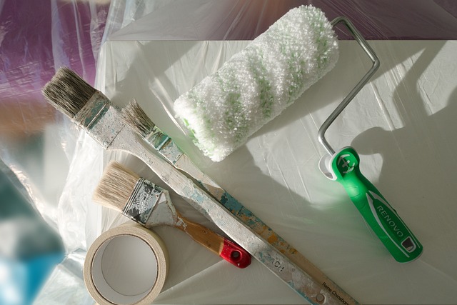 Painting supplies, including brushes, paint tubes, and a roll of plastic wrap, arranged on a table.