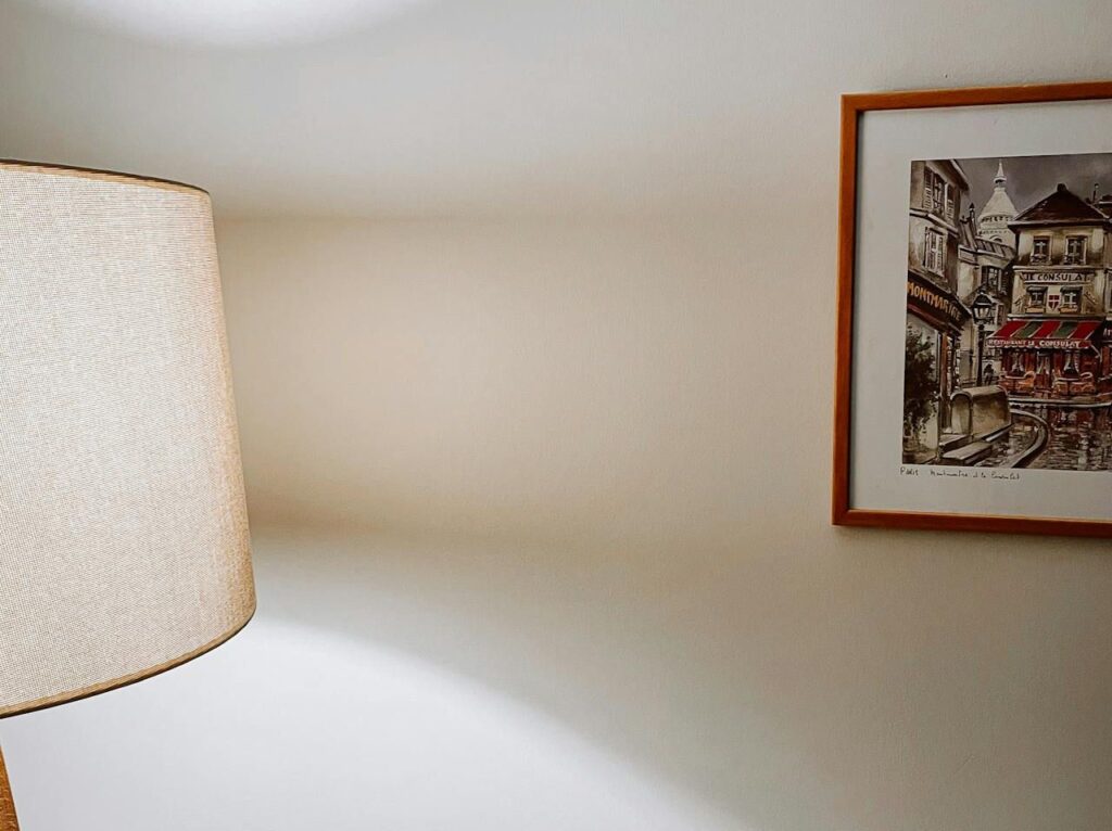 A lamp and a picture on a table, with non-pasted wallpaper in the background.