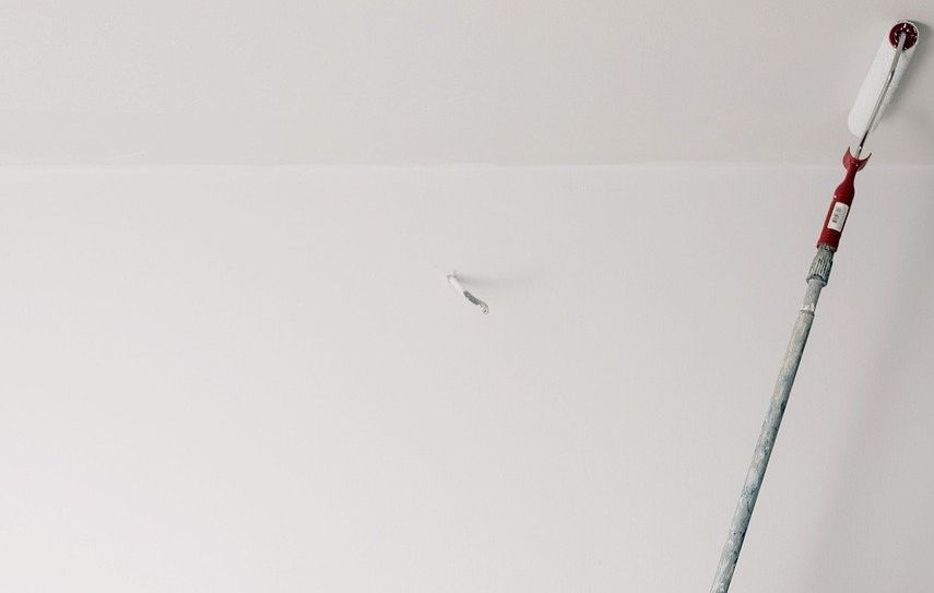 A white wall with a paint brush and a paint can. Image illustrating how to remove adhesive from a wall.